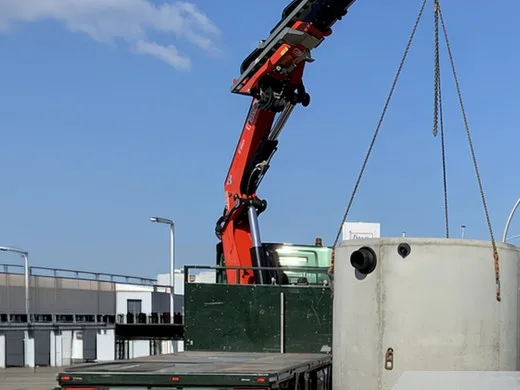 Levering van een vetafscheider: kraan hijst een betonnen put van de trailer