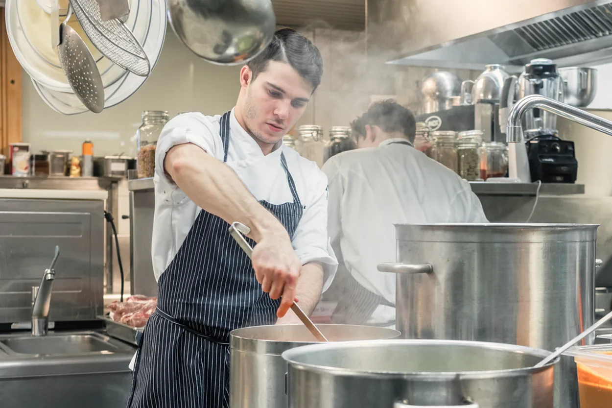 Kok roert in grote pannen op het fornuis van een grootkeuken
